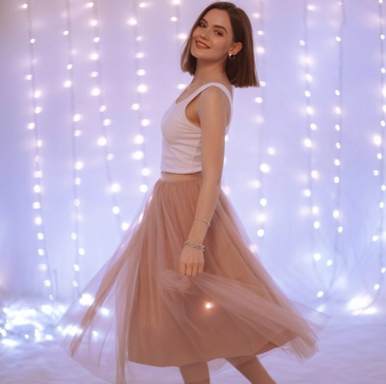 Dreamy studio backdrop with fairy lights. Model in a blush tulle midi skirt paired with a fitted white tank top, delicate heels, and subtle jewelry. Spinning gently, dreamy smile, ethereal vibe.
