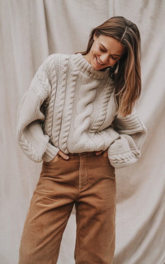 A natural-looking young woman wearing a cable knit sweater with corduroy pants. Theme winter fashion outfits