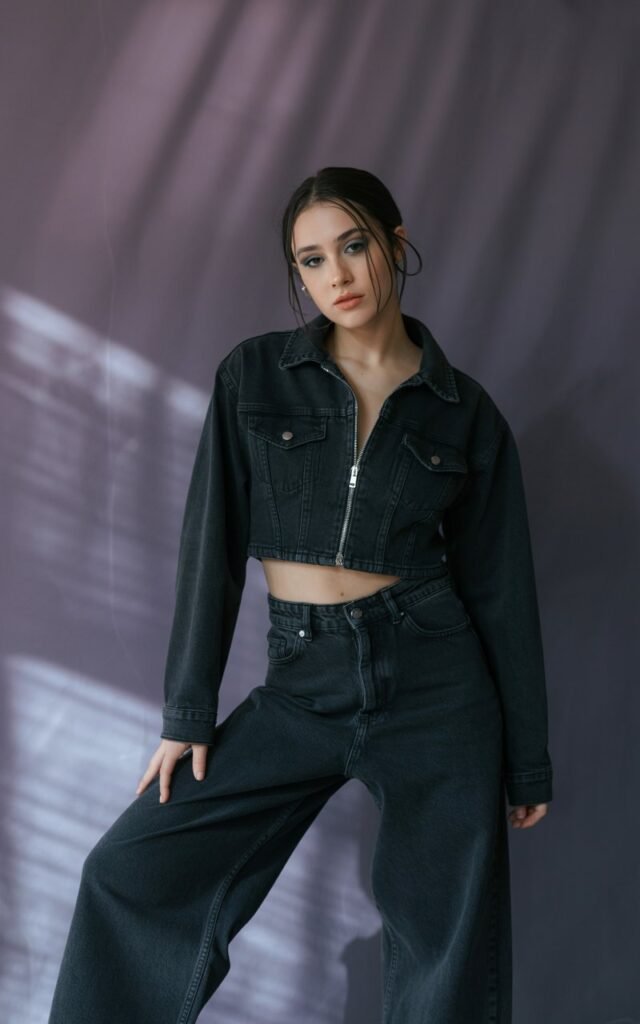 A natural-looking young woman wearing a cropped jacket paired with wide-leg black jeans. Theme emo outfits