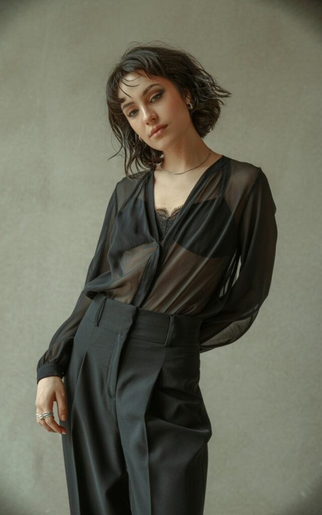 A natural-looking young woman wearing a flowy black top balanced with structured black pants. Theme emo outfits