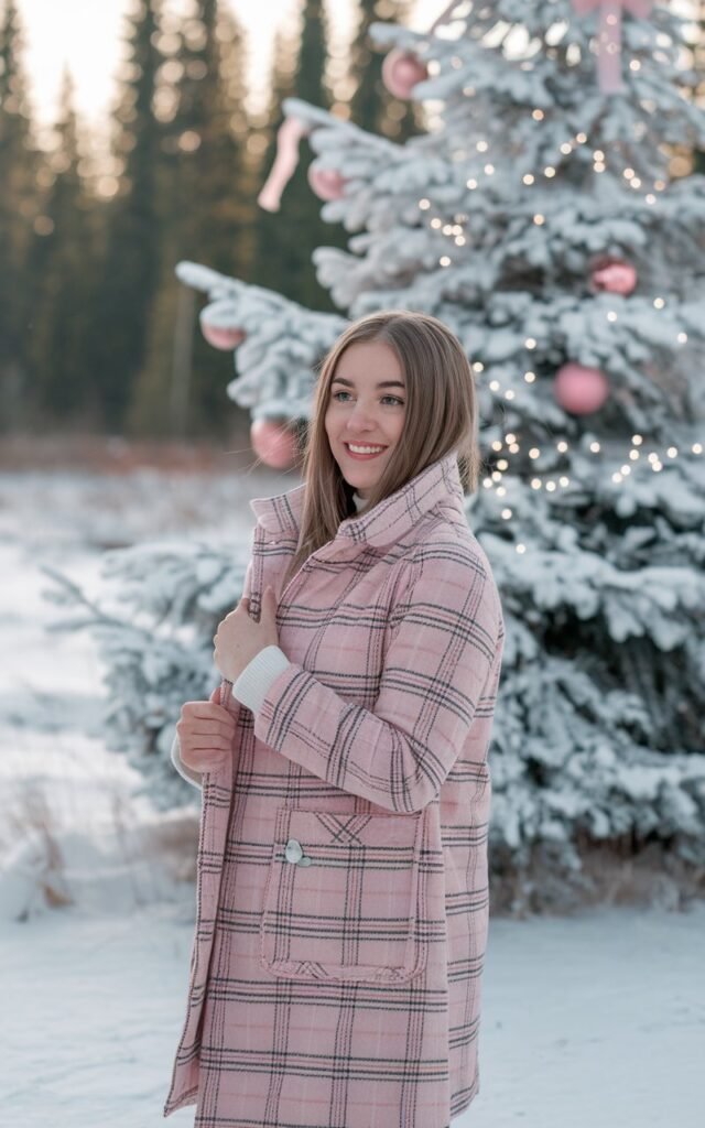 A natural-looking young woman wearing a pink plaid coat styled with winter white pieces. Theme pink christmas outfit