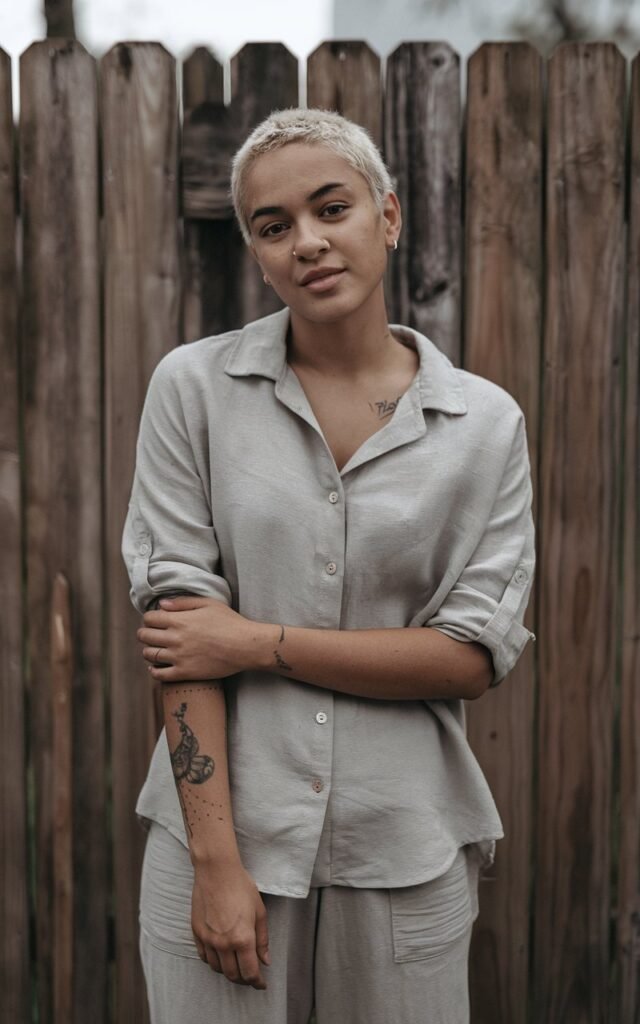 A natural-looking young woman wearing a simple button-down shirt with sleeves rolled up and relaxed-fit pants. Theme tomboy outfits