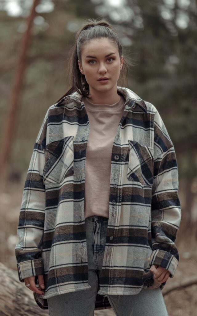 A natural-looking young woman wearing an oversized flannel layered over a solid tee with casual jeans. Theme tomboy outfits
