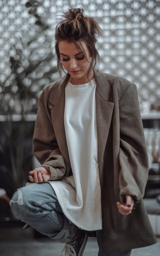 A natural-looking young woman wearing an oversized white tee layered under a structured blazer with sneakers. Theme tomboy outfits