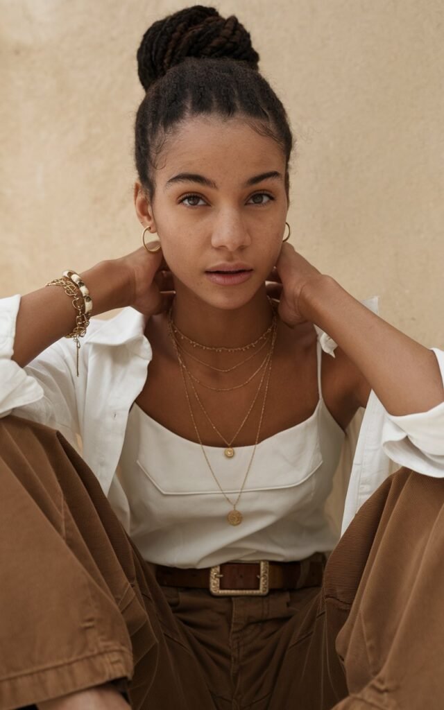 A natural-looking young woman wearing brown pants accessorized with gold jewelry for a refined and trendy finish. Theme brown pants outfit for women