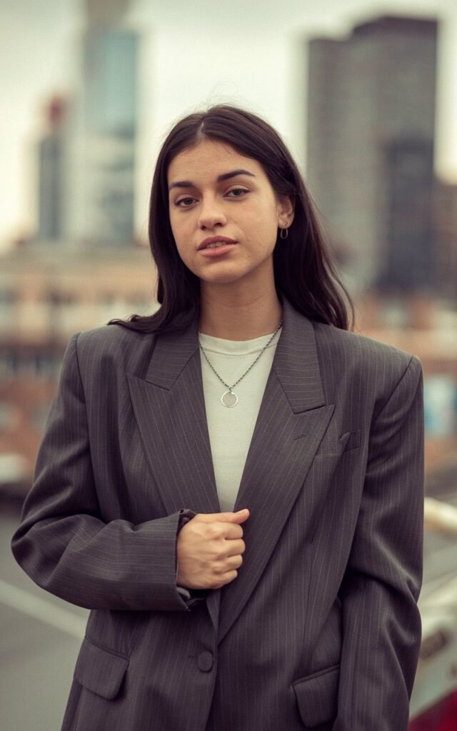 A natural-looking young woman wearing a sharp shoulder-pad blazer styled for power dressing. Theme 80s outfits