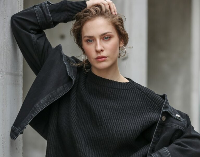 A natural-looking young woman wearing an all-black outfit with mixed textures like knit, leather, and denim. Theme stylish outfits