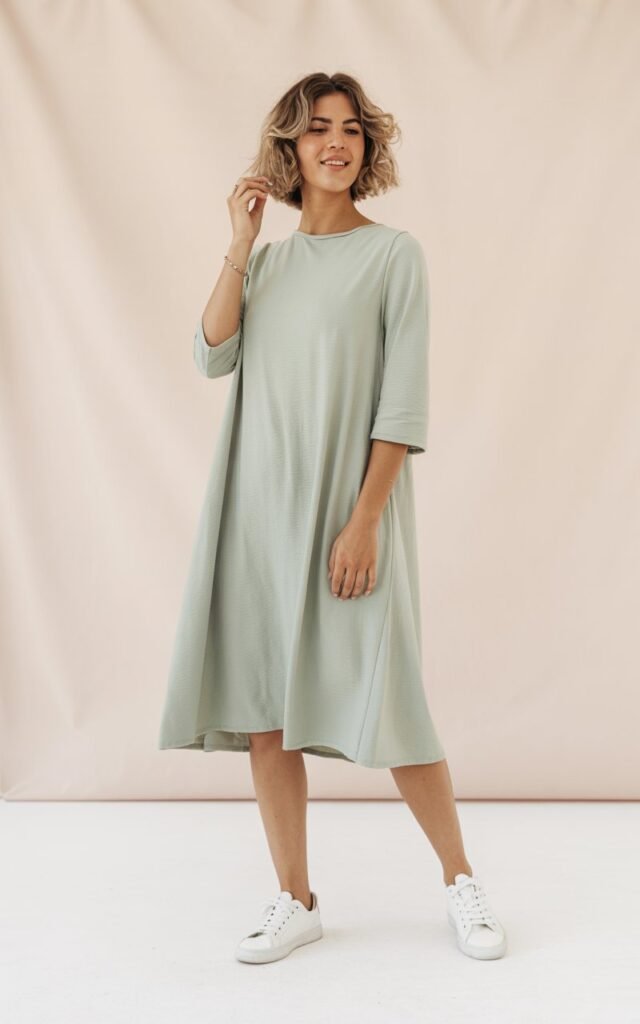 A natural-looking young woman wearing a flowy midi dress paired with clean white sneakers. Theme lookbook outfits